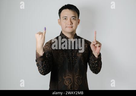 Ein asiatischer Mann mit Batiktuch zeigt seinen kleinen Finger mit violetter Tinte, um nach Pemilu oder Indonesien die Nummer eins zu wählen Stockfoto