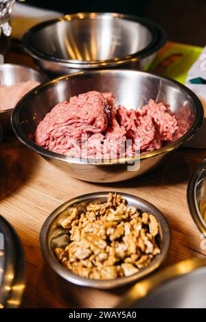 Rohes Hackfleisch zum Kochen und eine Schüssel Walnüsse als Zutaten auf einer warmen hölzernen Küchenoberfläche. Stockfoto