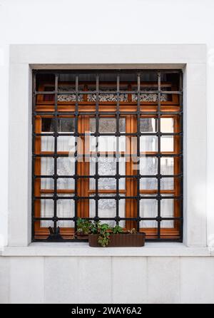 Fenster mit Eisengitter an weißer Wand. Gitter am Fenster, Architektur eines Landhauses. Fensterleisten. Über dem Fenster montierte Leisten. Niemand, stree Stockfoto