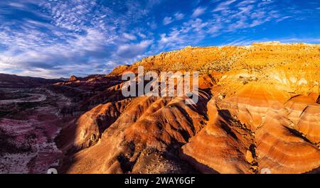 Eine trockene Wüstenlandschaft, beleuchtet von den goldenen Tönen der Nachmittagssonne, während flauschige weiße Wolken am Himmel hängen Stockfoto