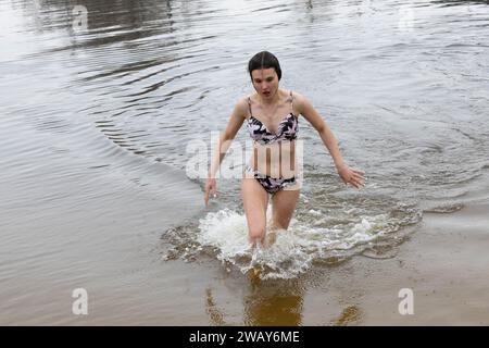 Kiew, Ukraine. Januar 2024. Eine Frau kommt aus dem Wasser, nachdem sie im kalten Fluss Dnipro geschwommen ist, anlässlich der Feier der Epiphanik in Kiew. Die Ukraine feiert in diesem Jahr erstmals die Epiphanik am 6. Januar nach dem westlichen Kalender und weicht von der Tradition der russisch-orthodoxen Kirche ab, sie am 19. Januar zu feiern. Während der Epiphanienzeit glauben manche, dass das Wasser besondere heilende Eigenschaften hat und zur Behandlung verschiedener Krankheiten verwendet werden kann, und viele von ihnen nehmen im Rahmen der Epiphanienfeier ein Bad im Wasser. (Kreditbild: © Oleksii Chumachenko/SOPA Images Via Stockfoto