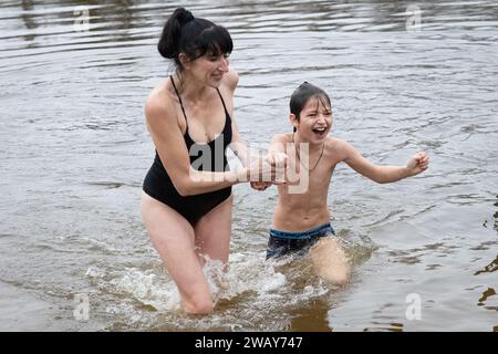 Kiew, Ukraine. Januar 2024. Eine Frau und ihr Sohn schwimmen in kalten Gewässern des Dnipro-Flusses anlässlich der Feier der Epiphanik in Kiew. Die Ukraine feiert in diesem Jahr erstmals die Epiphanik am 6. Januar nach dem westlichen Kalender und weicht von der Tradition der russisch-orthodoxen Kirche ab, sie am 19. Januar zu feiern. Während der Epiphanienzeit glauben manche, dass das Wasser besondere heilende Eigenschaften hat und zur Behandlung verschiedener Krankheiten verwendet werden kann, und viele von ihnen nehmen im Rahmen der Epiphanienfeier ein Bad im Wasser. (Credit Image: © Oleksii Chumachenko/SOPA Images via ZUMA Press Stockfoto