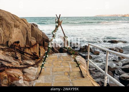 Dreieck-Hochzeitsbogen mit Blumen an einem felsigen Strand in Bulgarien. Wunderschönes Hochzeitskonzept am Meer. Stockfoto