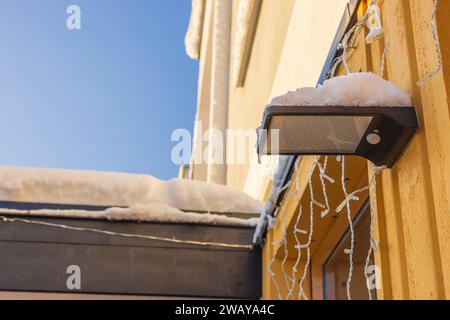 Detaillierte Ansicht der Außenleuchte mit schneebedecktem Solarpanel an der Fassade der Villa an einem frischen Wintertag. Schweden. Stockfoto