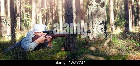 Ein Mann liegt auf dem Boden im Wald und zielt mit einem Luftgewehr. Das Konzept ist ein Hobby, viel Spaß im Wald und eine Ausbildung zum Schützen. Stockfoto