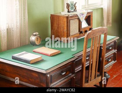 Vintage-Schreibtisch in grüner Materialoberfläche bei Tageslicht durch Fenster mit vielen Schubladen und altem Radio und Uhr drauf. Stockfoto