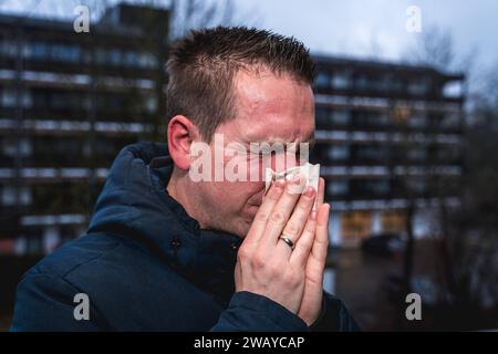 Bayern, Deutschland - 6. Januar 2024: Ein kranker Mann mit Erkältung bläst sich mit einem Papiertaschentuch die Nase *** ein kranker erkälteter Mann putzt sich mit einem Papiertaschentuch die Nase Stockfoto