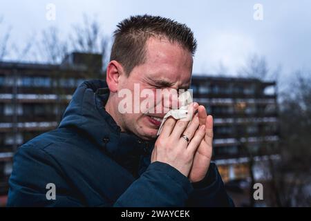 Bayern, Deutschland - 6. Januar 2024: Ein kranker Mann mit Erkältung bläst sich mit einem Papiertaschentuch die Nase *** ein kranker erkälteter Mann putzt sich mit einem Papiertaschentuch die Nase Stockfoto