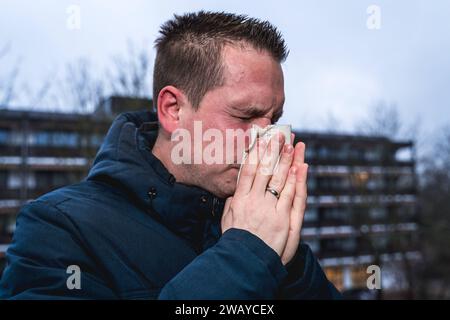 Bayern, Deutschland - 6. Januar 2024: Ein kranker Mann mit Erkältung bläst sich mit einem Papiertaschentuch die Nase *** ein kranker erkälteter Mann putzt sich mit einem Papiertaschentuch die Nase Stockfoto