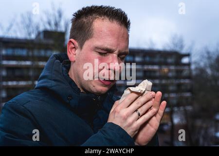 Bayern, Deutschland - 6. Januar 2024: Ein kranker Mann mit Erkältung bläst sich mit einem Papiertaschentuch die Nase *** ein kranker erkälteter Mann putzt sich mit einem Papiertaschentuch die Nase Stockfoto