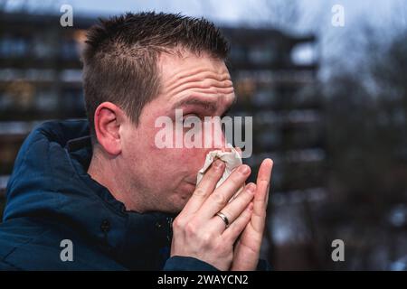 Bayern, Deutschland - 6. Januar 2024: Ein kranker Mann mit Erkältung bläst sich mit einem Papiertaschentuch die Nase *** ein kranker erkälteter Mann putzt sich mit einem Papiertaschentuch die Nase Stockfoto