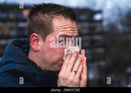 Bayern, Deutschland - 6. Januar 2024: Ein kranker Mann mit Erkältung bläst sich mit einem Papiertaschentuch die Nase *** ein kranker erkälteter Mann putzt sich mit einem Papiertaschentuch die Nase Stockfoto