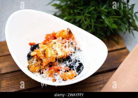 Italienische Penne-Pasta, gemischt mit einer reichhaltigen Tomatensauce, schwarzen Oliven und bestreut mit geriebenem Käse in einer modernen weißen Schüssel. Stockfoto