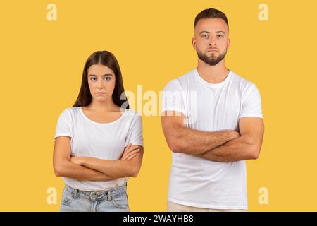 Sterngesichtiges junges Paar mit überkreuzten Armen in weißen T-Shirts, das ein starkes Gefühl von Meinungsverschiedenheiten ausstrahlt Stockfoto