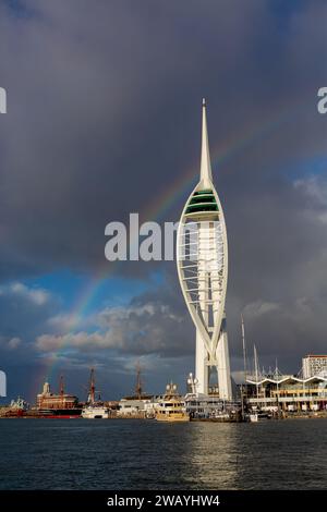 Spinnaker Tower in Portsmouth, der bei direktem Sonnenlicht mit dunkler bewölkter Kulisse herrlich aussieht. Großer Regenbogenbogen, der sich mit dem oberen Dorn schneidet. Stockfoto