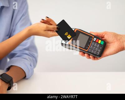 Nahaufnahme der Hände Halten Sie die schwarze kontaktlose Kreditkarte über den Kartenleser, um die Zahlung abzuschließen Stockfoto
