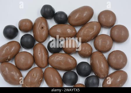 Schokolade in verschiedenen Größen, Erdnüsse, Nüsse, Rosinen sind mit Milchschokolade und dunkler Schokoladenglasur bedeckt, Kieselsteine auf weißem Hintergrund Stockfoto