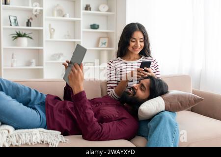 Entspanntes junges indisches Paar, das zu Hause Gadgets benutzt Stockfoto