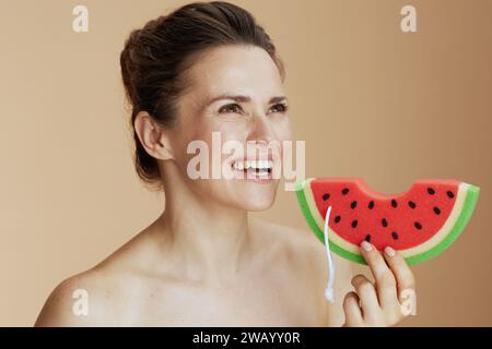 Glückliche moderne Frau mit Wassermelonen-Duschschwamm auf beigem Hintergrund. Stockfoto