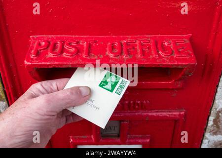 Einen Brief der zweiten Klasse in einem roten Briefkasten der Royal Mail verschicken. Stockfoto