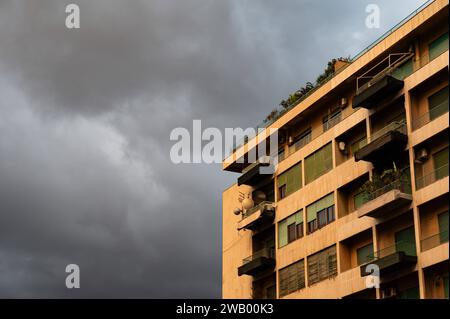 Palmero, Sizilien, Italien, 16. Dezember 2023 - Gelber Wohnblock vor dunklen, regnerischen Wolken Stockfoto