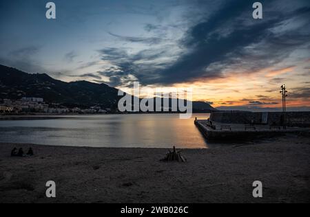 Cefalu, Sizilien, Italien, 19. Dezember 2023 - Sonnenuntergang von den Docks über dem Meer und den Bergen des Dorfes Stockfoto