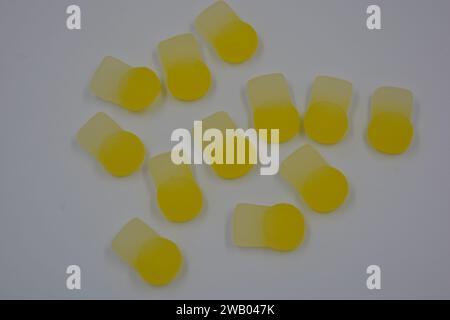 Gebrandete, werkseitig hergestellte gummiartige Kinderbonbons in Form von kleinen Früchten, Orangen, gelben Beeren, die auf weiß angeordnet sind. Stockfoto