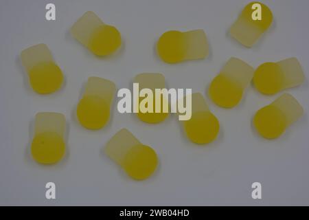 Gebrandete, werkseitig hergestellte gummiartige Kinderbonbons in Form von kleinen Früchten, Orangen, gelben Beeren, die auf weiß angeordnet sind. Stockfoto