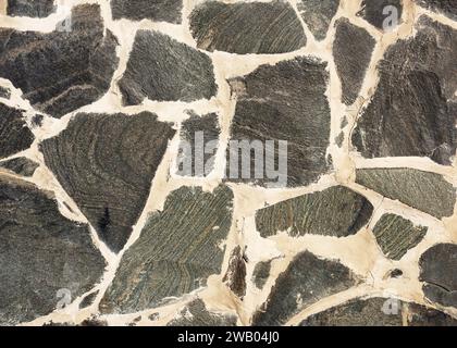Alte dunkelgraue rustikale Mosaik Natur Steinmauer aus verschiedenen Größen und Formteilen. Vintage-Dekorationselemente. Abstraktes geometrisches Muster Stockfoto