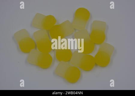 Gebrandete, werkseitig hergestellte gummiartige Kinderbonbons in Form von kleinen Früchten, Orangen, gelben Beeren, die auf weiß angeordnet sind. Stockfoto