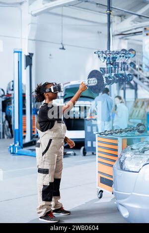 Qualifizierter Ingenieur in der Werkstatt, der VR-Brillen und Augmented Reality-Hologramm verwendet, um Autoteile zu visualisieren und zu reparieren. BIPOC-Frau, die AR-Technologie verwendet, während sie an einem beschädigten Fahrzeugmotor arbeitet Stockfoto
