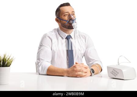 Nachdenklicher Mann, der auf einem Tisch sitzt und einen Vernebler benutzt, der auf weißem Hintergrund isoliert ist Stockfoto