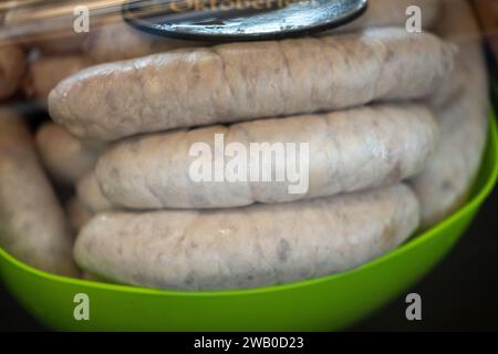 Eine grüne Plastikschale gefüllt mit Oktoberfestwürsten in einer Vitrine mit schwarzem Schild und goldenen Buchstaben. Das ungekochte Protein ist roh. Stockfoto