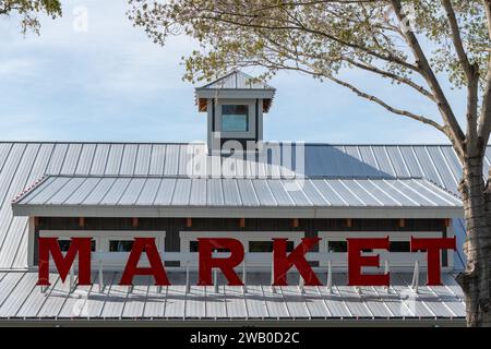 Ein leuchtendes rot beleuchtetes Marktschild auf dem Dach eines rustikalen Gebäudes. Die Ladenfront hat ein Dach mit Spitze, ein großes Fenster und eine hölzerne Außenwand. Stockfoto