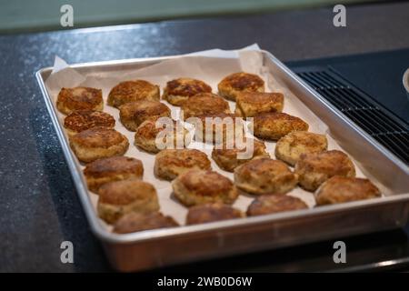 Ein Tablett mit gekochtem, rundem Salzjau-Fischkuchen, zubereitet auf einem Grill. Die Mischung aus Bohnenkraut, Kartoffeln, Kabeljau und Butter wird zu kleinen Patties geformt Stockfoto