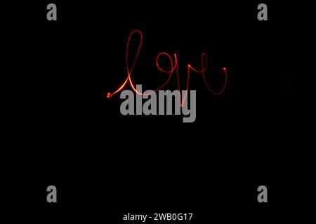 Die Liebe wird kursiv geschrieben, indem sie mit einer langen Verschlusszeit das Wort auf dem schwarzen Hintergrund belichtet. Stockfoto