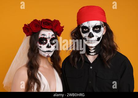 Ein Paar in gruseligen Braut- und Piratenkostümen auf orangem Hintergrund. Halloween-Feier Stockfoto