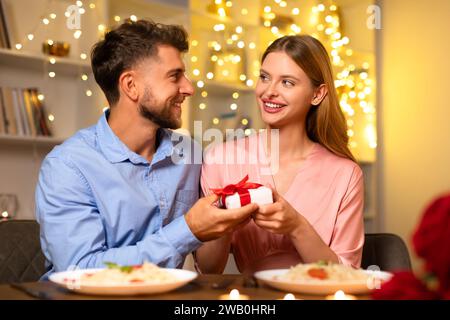 Mann, der glücklichen Frau ein Geschenk gibt, beide lächeln beim Essen Stockfoto