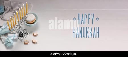 Happy Hanukkah. Menora, Donut, Dreidels und Geschenke auf weißem Holztisch, Banner-Design Stockfoto