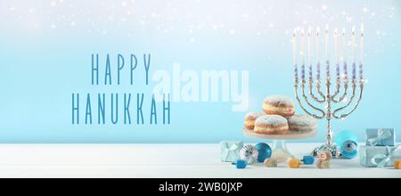 Happy Hanukkah. Menora, Donuts, Dreidels und Geschenke auf weißem Tisch, Banner-Design Stockfoto