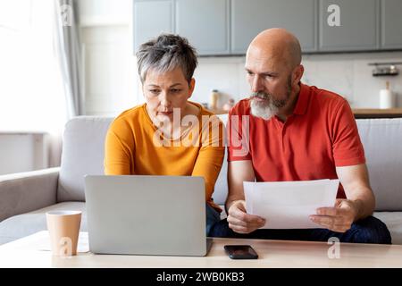 Ältere Ehepartner Lesen Papiere Und Benutzen Zu Hause Einen Laptop Stockfoto