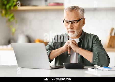 Nachdenklicher älterer Mann mit Brille und Laptop zu Hause Stockfoto
