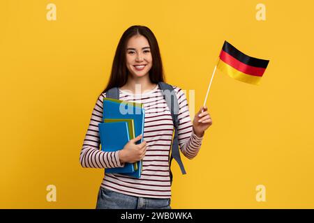 Glückliche junge asiatische Studentin, die die Flagge Deutschlands zeigt Stockfoto