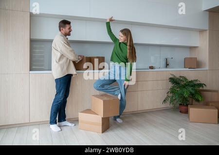 Glückliches müdes, junges Familienpaar, das in der Küche zwischen Kisten spricht und in eine neue Wohnung zieht. Stockfoto