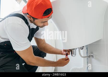 Mit einem Schraubenschlüssel in der Hand fixiert ein Techniker eine Wasserleitung unter einem Waschbecken im Badezimmer. Dieser Klempnerservice Stockfoto