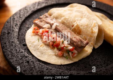 Tacos de Arrachera. Hausgemachtes gegrilltes Fleisch in einer Weizentortilla serviert auf einer vulkanischen Lavaplatte. Street Food aus Mexiko, traditionell begleitet von Stockfoto