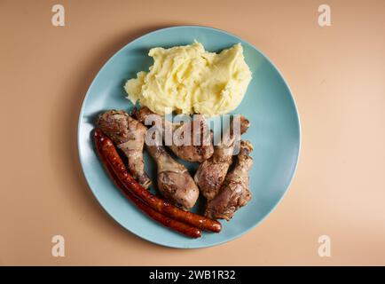 Gegrillte Hähnchenschenkel und Würstchen mit Kartoffelpüree auf einer blauen Platte isoliert auf beigem Hintergrund Stockfoto