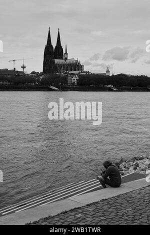 Blick über den Rhein mit Dom und einsamer Person davor, schwarz-weiß, Köln, Deutschland Stockfoto