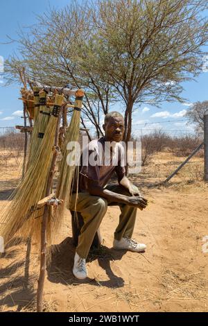 Straßenverkäufer im Dorf, afrikanischer Mann, der an einem sonnigen Tag an der Seite der Autobahn vor einem Besenständer steht Stockfoto