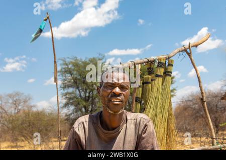 Straßenverkäufer im Dorf, afrikanischer Mann, der an einem sonnigen Tag an der Seite der Autobahn vor einem Besenständer steht Stockfoto